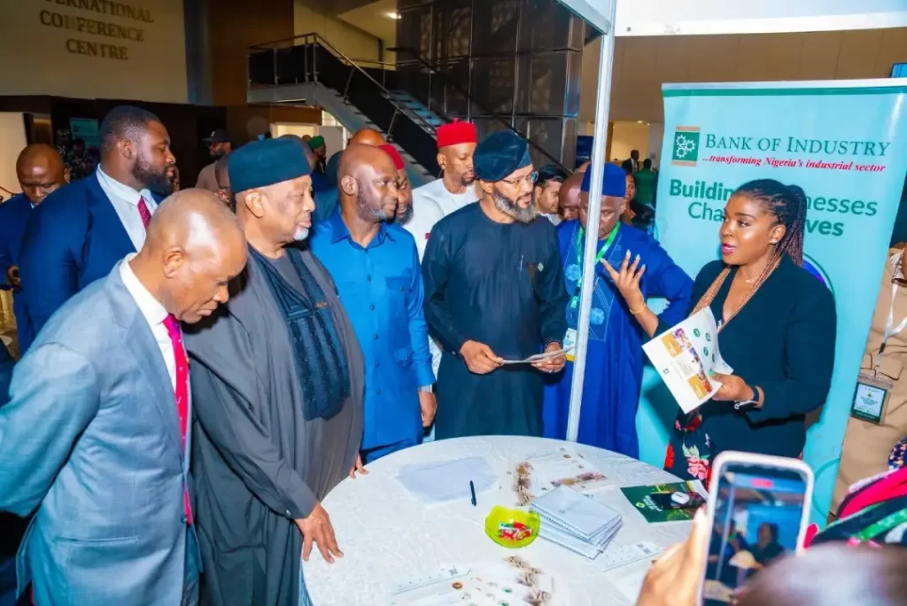 An exhibitor presenting value-addition materials to Dr. Olasupo Olusi, Senator John Owan Enoh, and delegates at the Bank of Industry pavilion