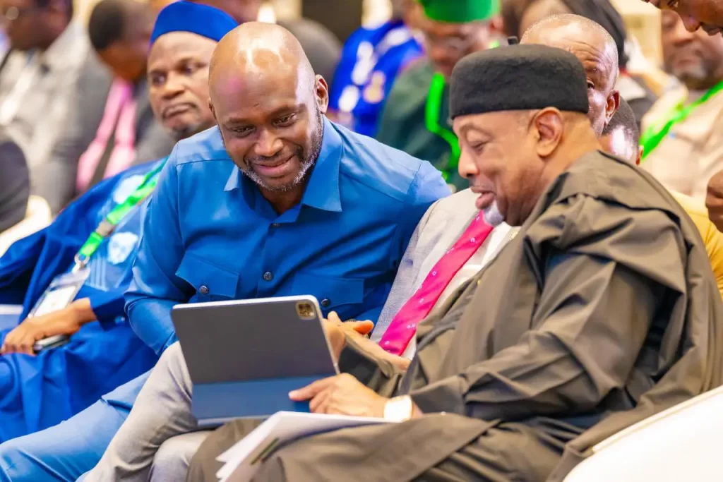Dr. Olasupo Olusi, MD/CEO of the Bank of Industry, leaning over to share content on a tablet with Senator Abubakar Kyari at the Cocoa Value Addition Summit